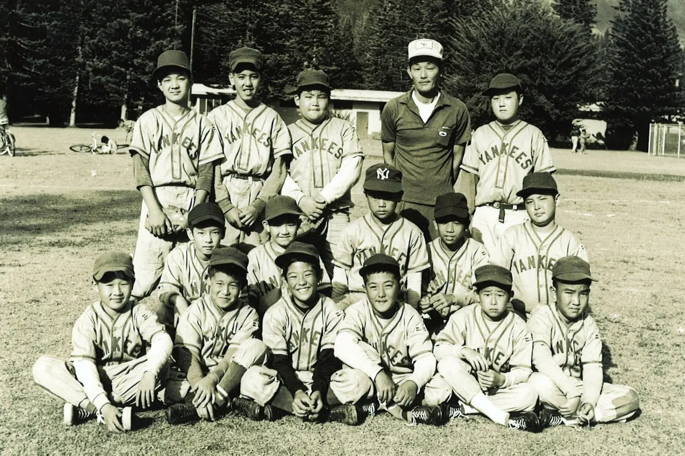 Black and white photo of the 1957 Lanai Midget League Champions: The proud baseball team poses together, showcasing their championship spirit with medals and smiles, a memorable moment in their historic victory.