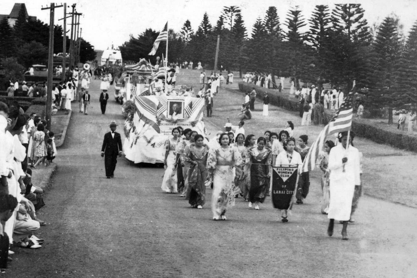 Black and white photograph of a lively parade featuring crowds of people marching down the street.