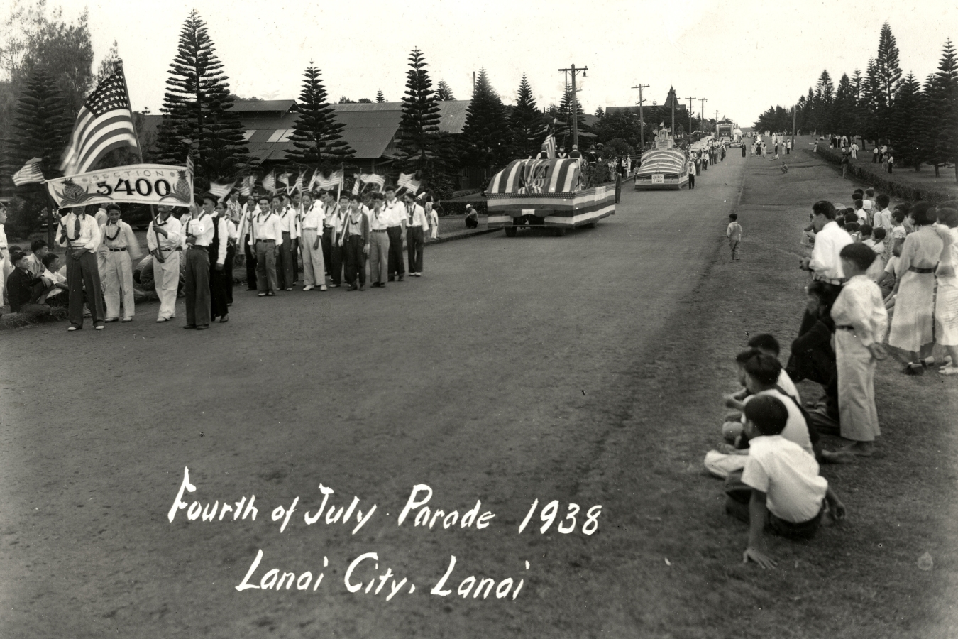 A monochrome photograph depicting a bustling parade with numerous individuals celebrating in the street.