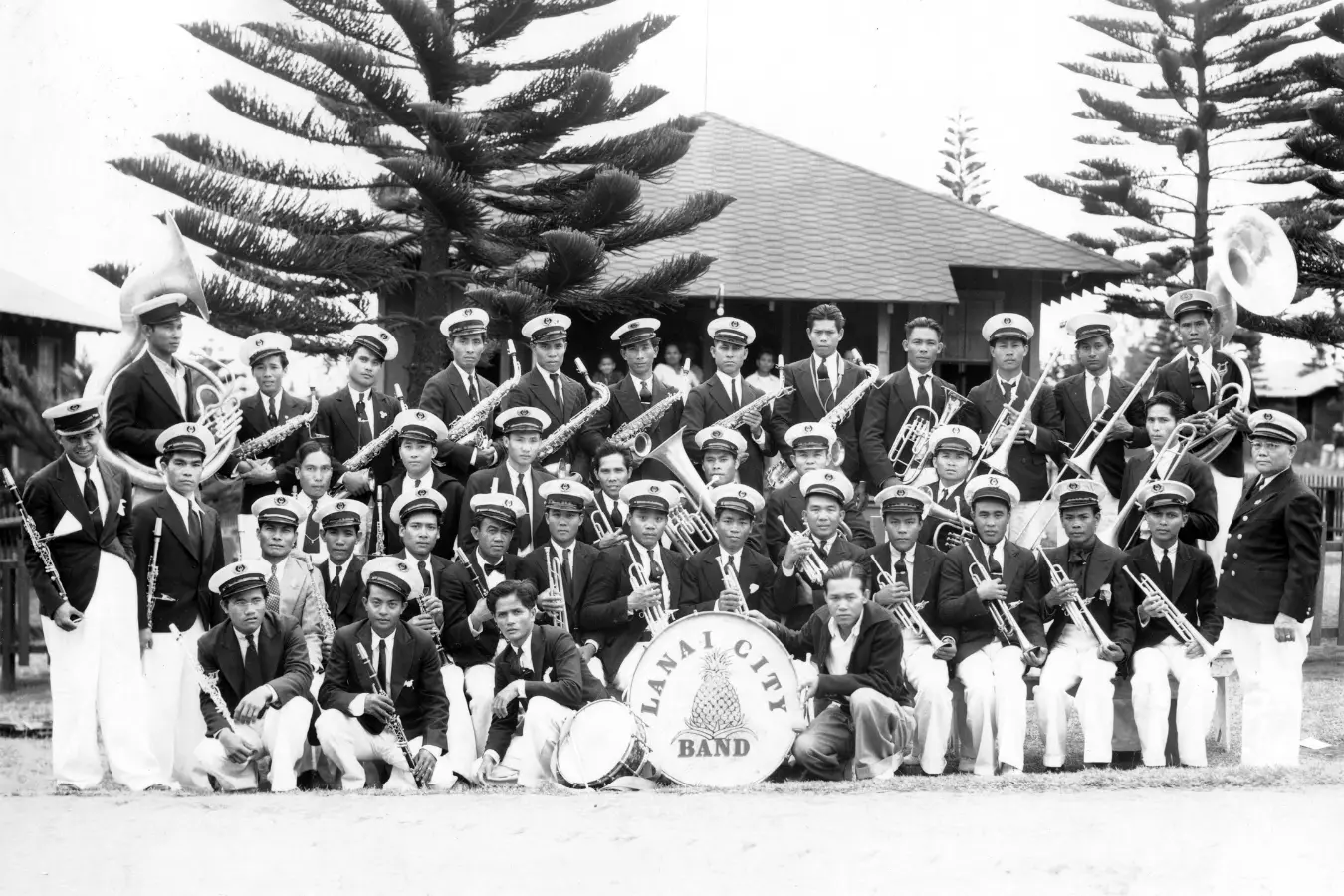 Black and white photo of the Lanai City Band, posed together for a group picture. The musicians, dressed in uniform, stand side by side, holding their instruments with pride, capturing a moment of unity and musical talent.