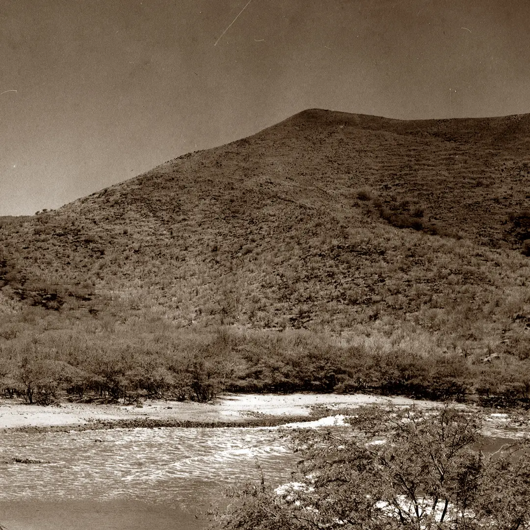 Old photo of a straight valley cutting through a mountain, with steep slopes on either side. The valley floor is lined with grass or vegetation, leading the eye toward the horizon, creating a striking natural corridor through the rugged terrain.