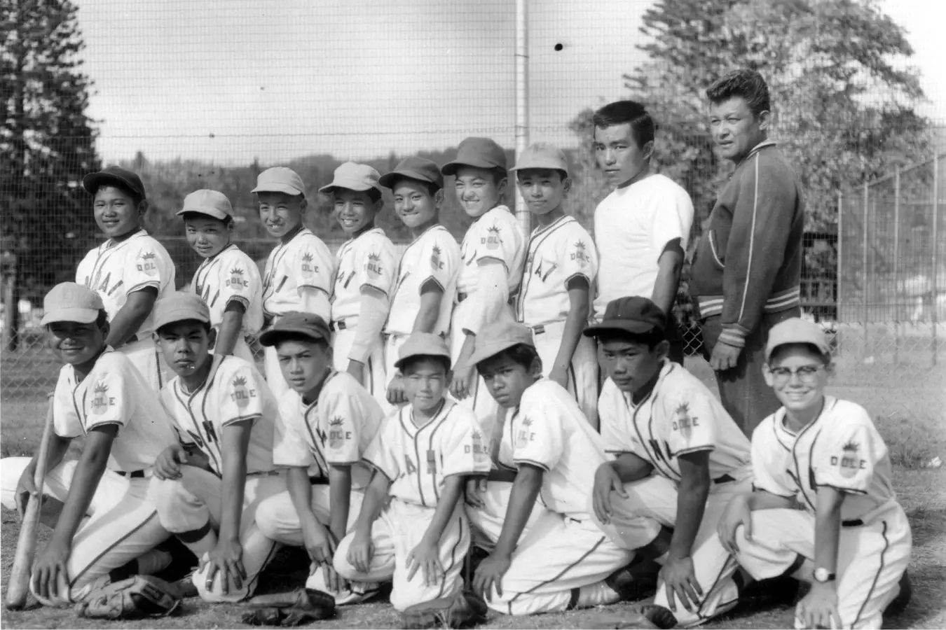 Black and white photo of a Little League baseball team smiling proudly with their coach for a team picture. The young players are dressed in their uniforms, standing together in a group, radiating team spirit and excitement.