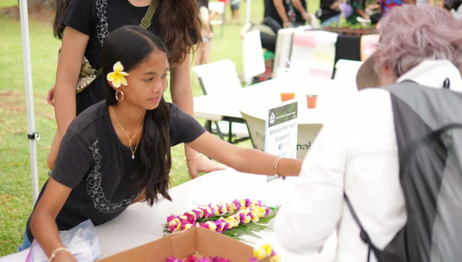 Girl sitting at the booth with lei.